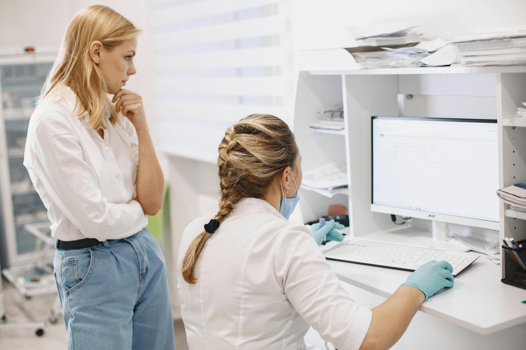 Two female healthcare workers collaborate in a clinic, analyzing data on a computer screen.